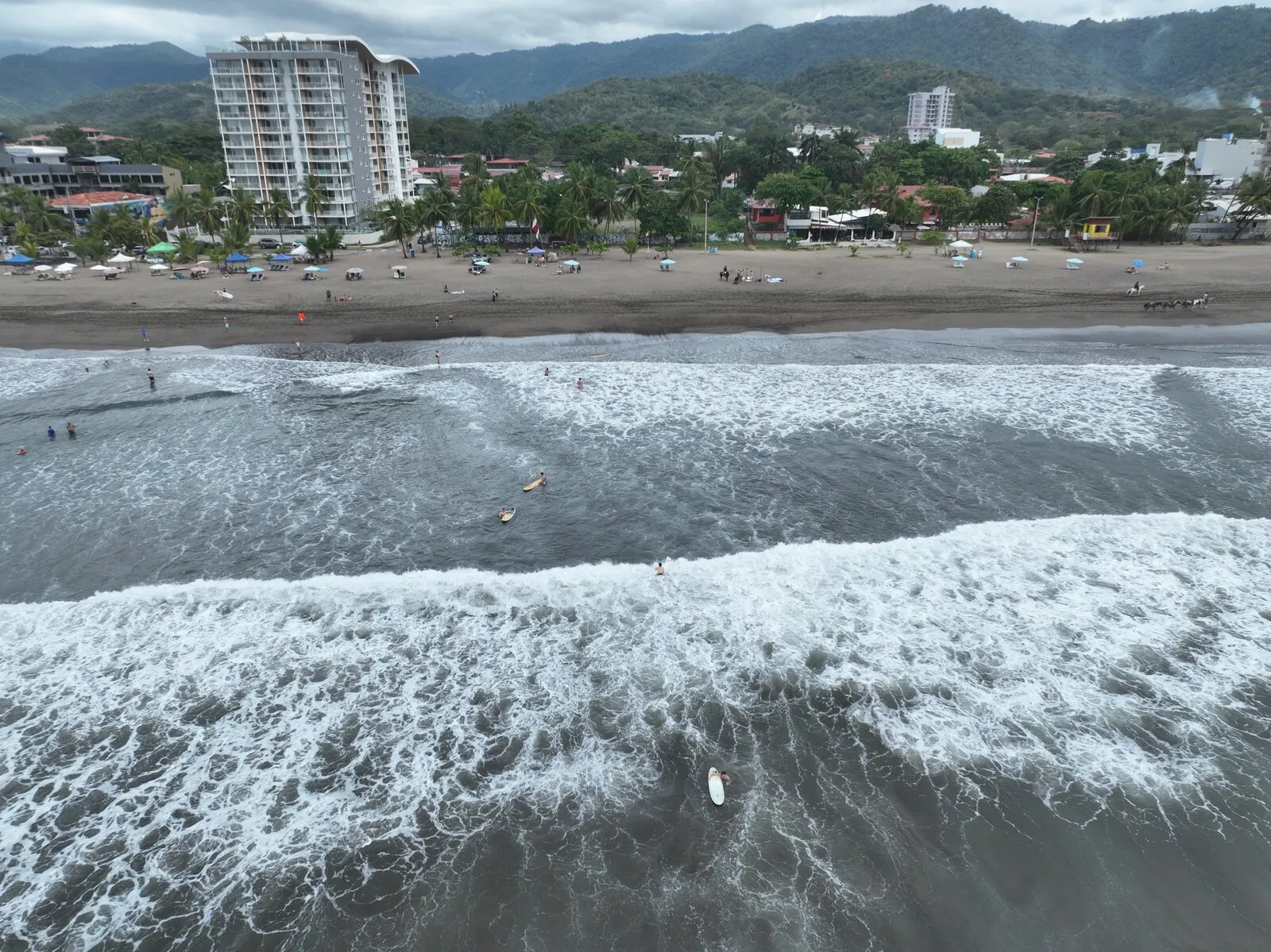 Surf rolling onto Jacó Beach, with the town behind (aerial)